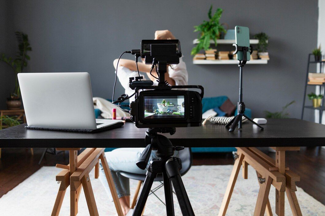 A person is sitting at a desk with a laptop and a camera on a tripod.